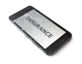 A smartphone with a severely cracked screen displays the word 'INSURANCE' on its screen. The device is black and appears to be placed on a white surface.