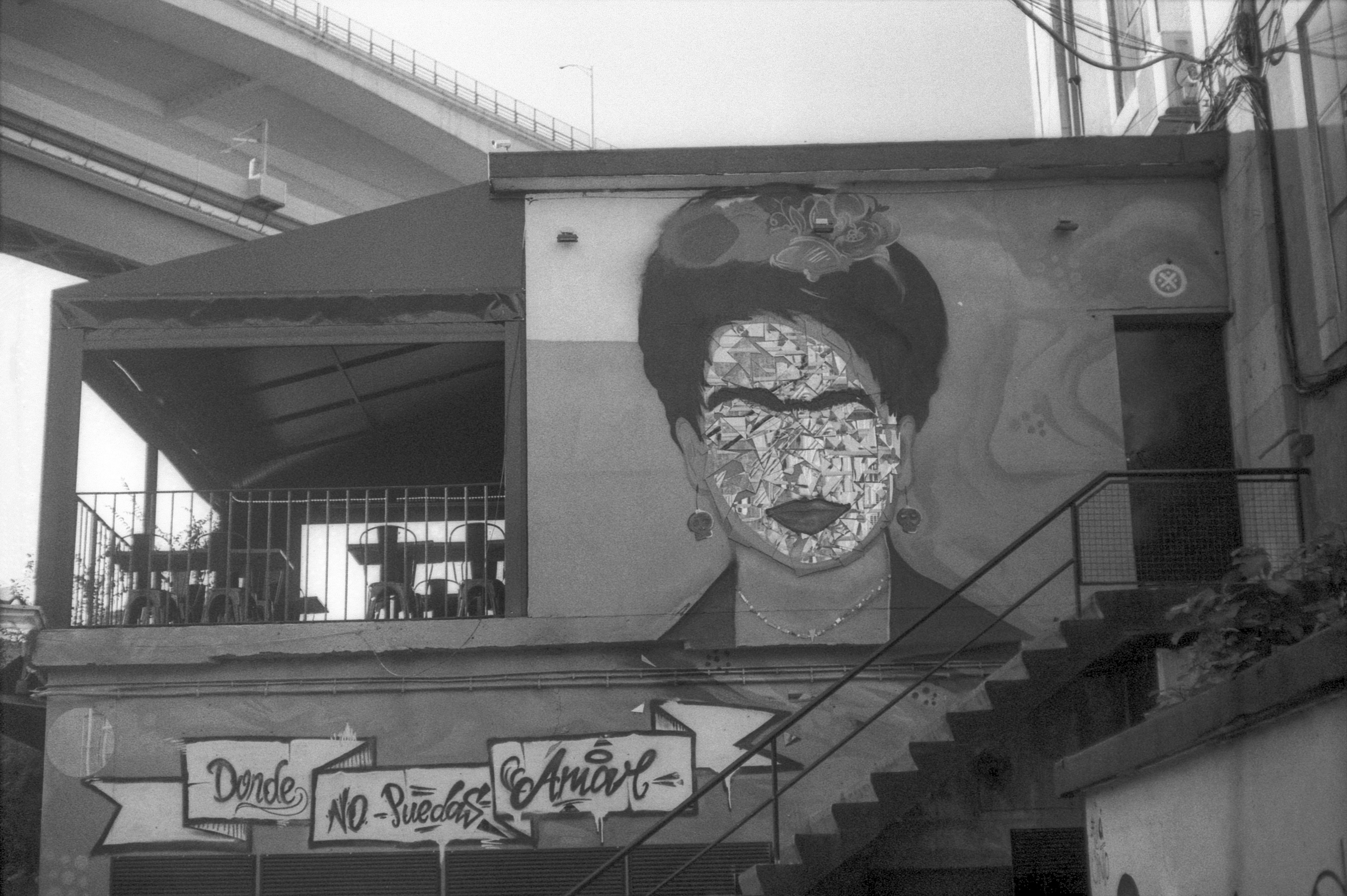 a black and white photo of a building with graffiti on it, Frida mural at the wall of a mexican restaurant