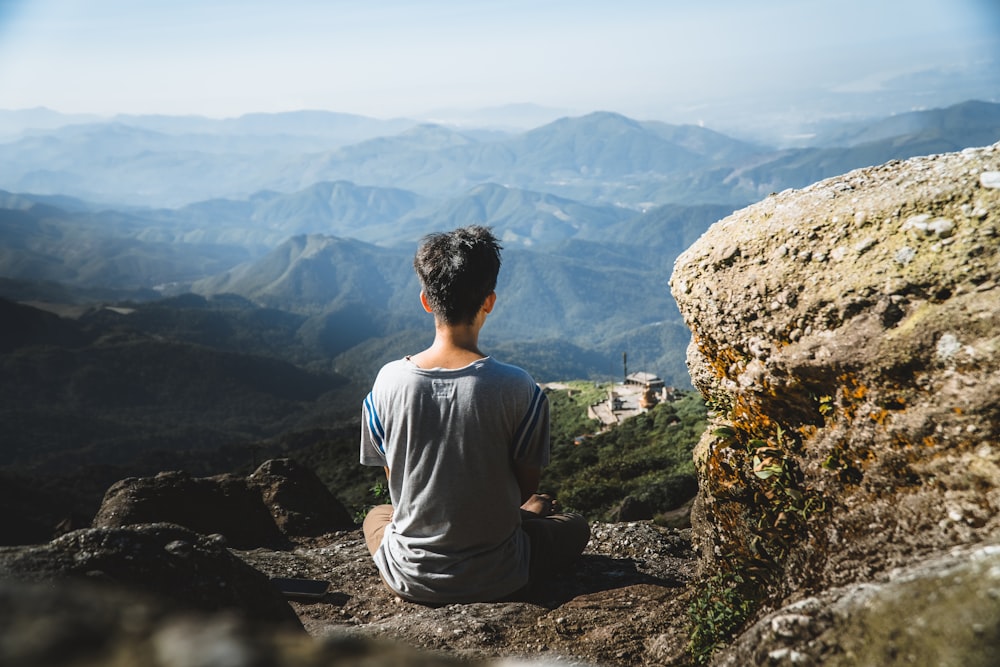 um homem sentado no topo de uma montanha olhando para as montanhas