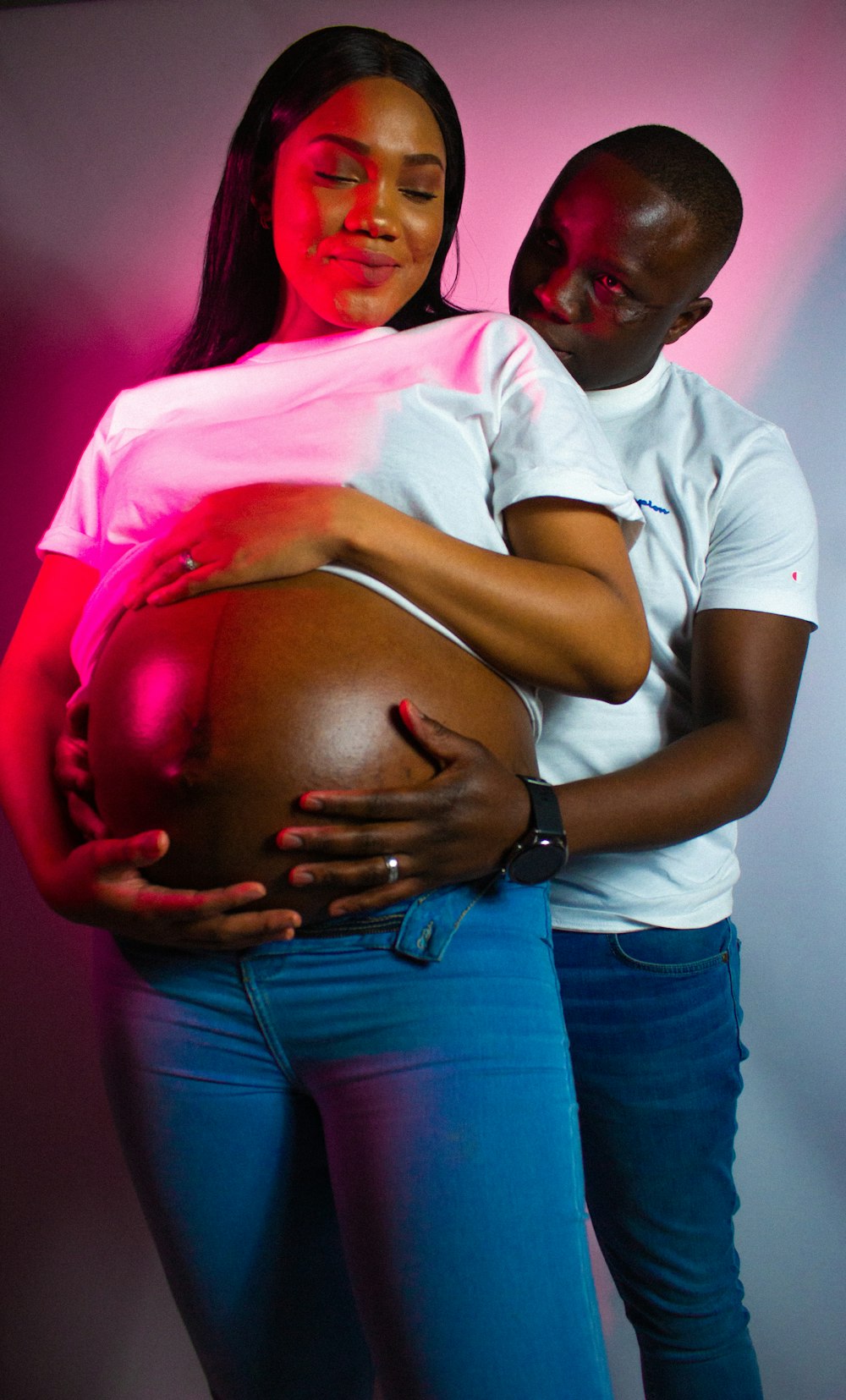 a pregnant woman hugging a man in a white t - shirt