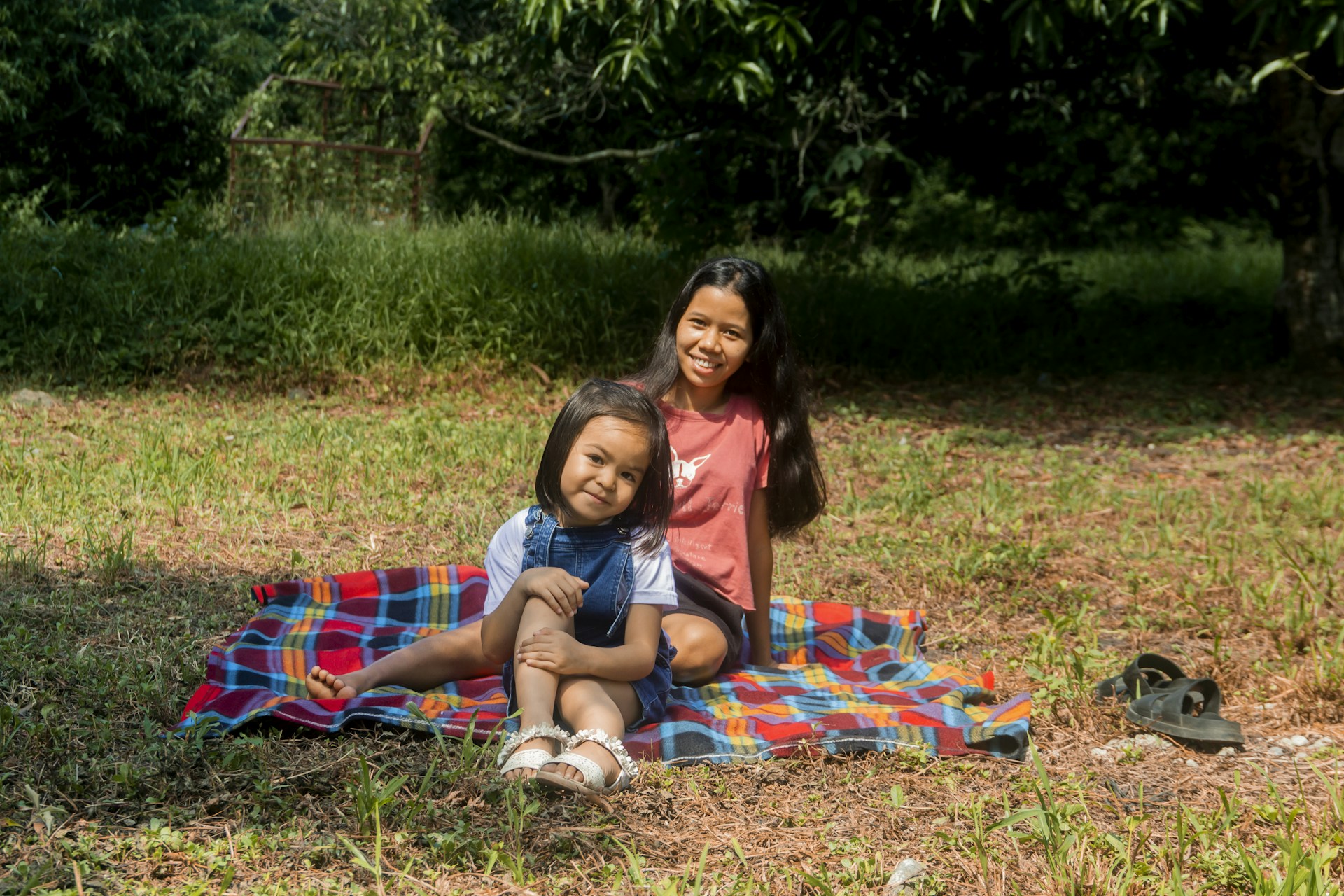 Two kids laughing together while drawing with crayons on a picnic blanket outdoors.