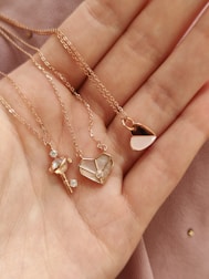 a woman's hand holding four different necklaces