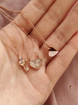 a woman's hand holding four different necklaces