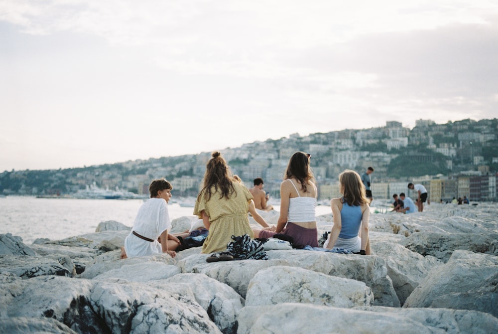 a group of people sitting on rocks near the water