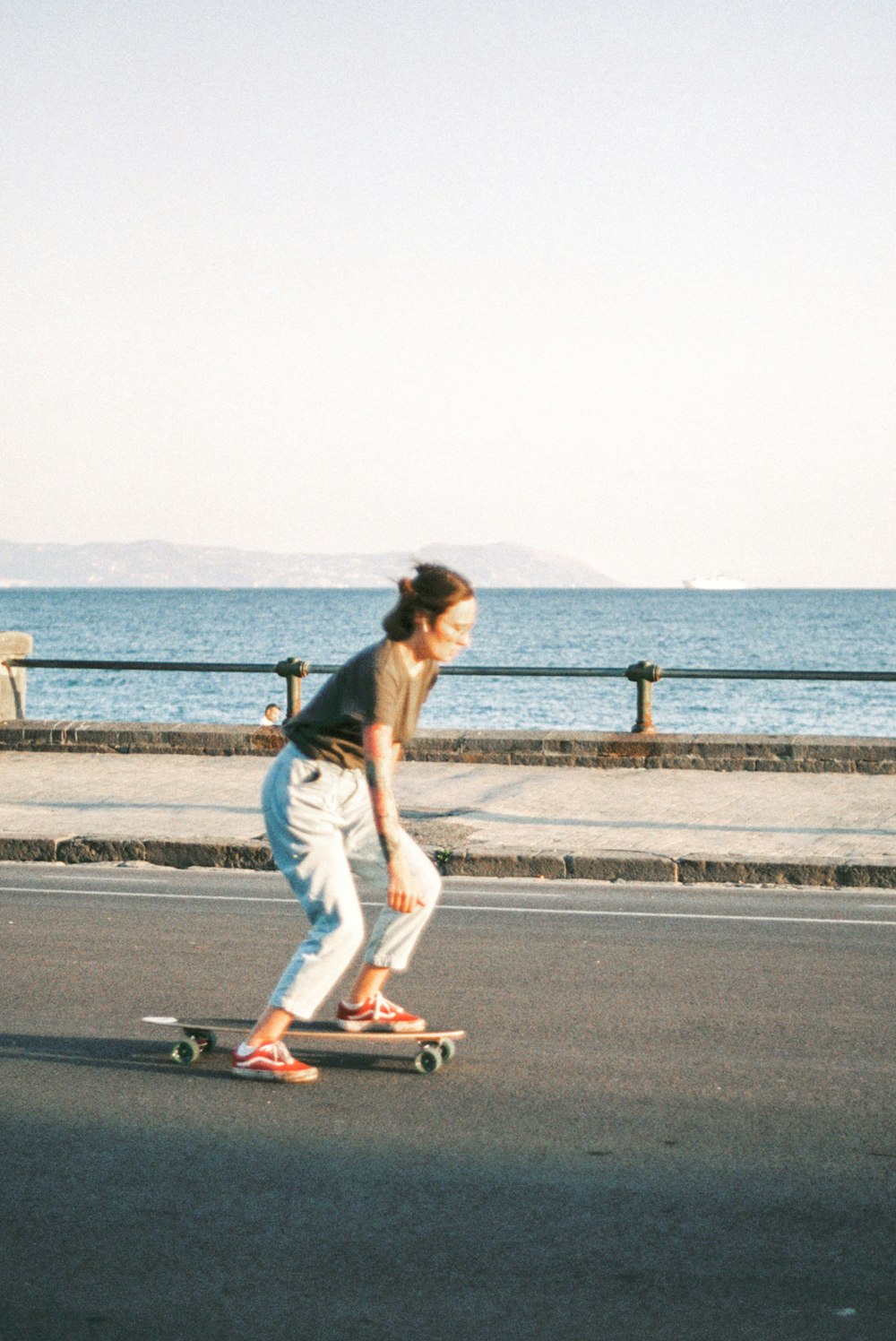 uma mulher andando de skate por uma rua ao lado do oceano