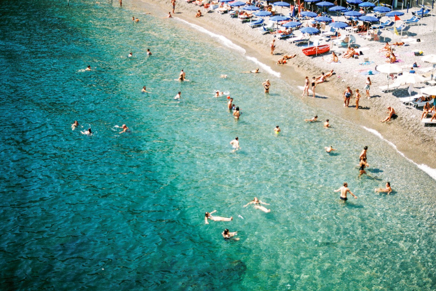 Swimmers in clear green water beside a row of parasols