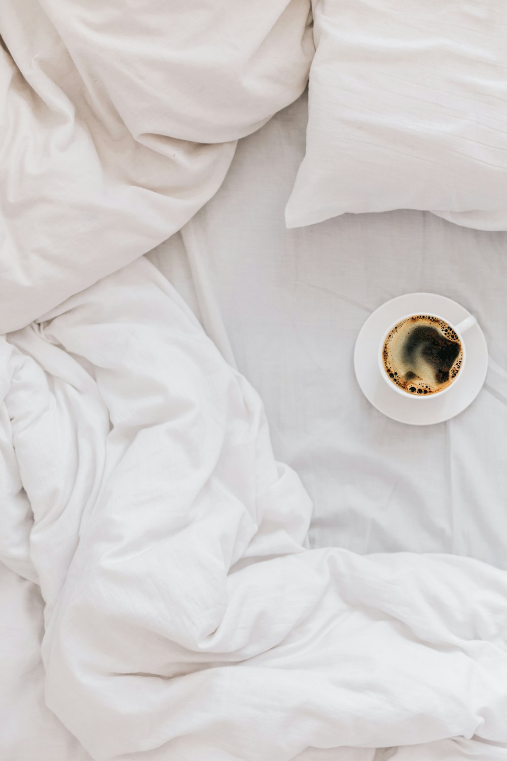 a cup of coffee sitting on top of a white bed