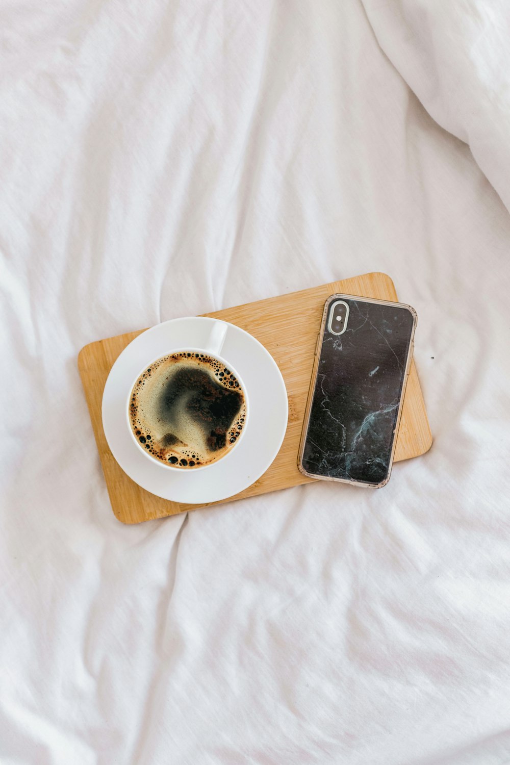 a cup of coffee and a cell phone on a bed