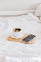 A mobile phone resting securely on a flexora stand beside a cozy coffee cup.