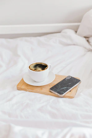 A mobile phone resting securely on a flexora stand beside a cozy coffee cup.
