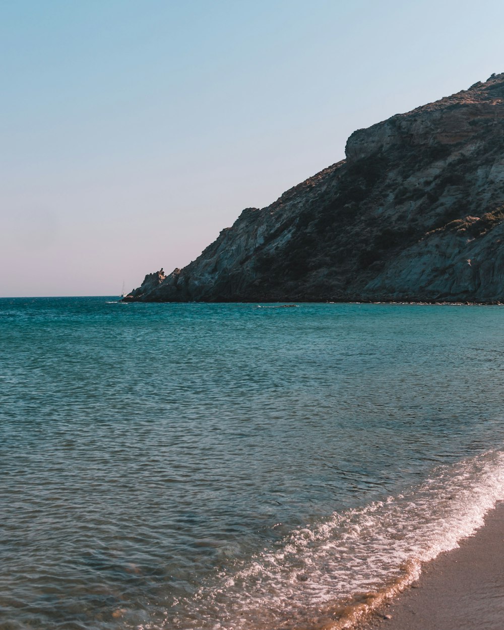 a sandy beach next to the ocean with a mountain in the background