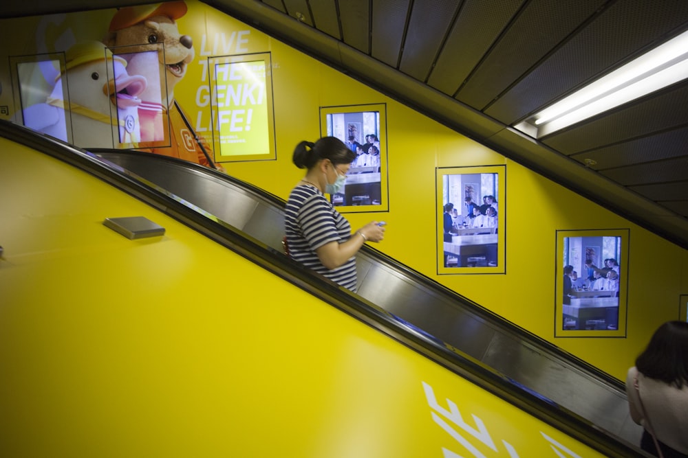 a woman riding an escalator down a yellow wall