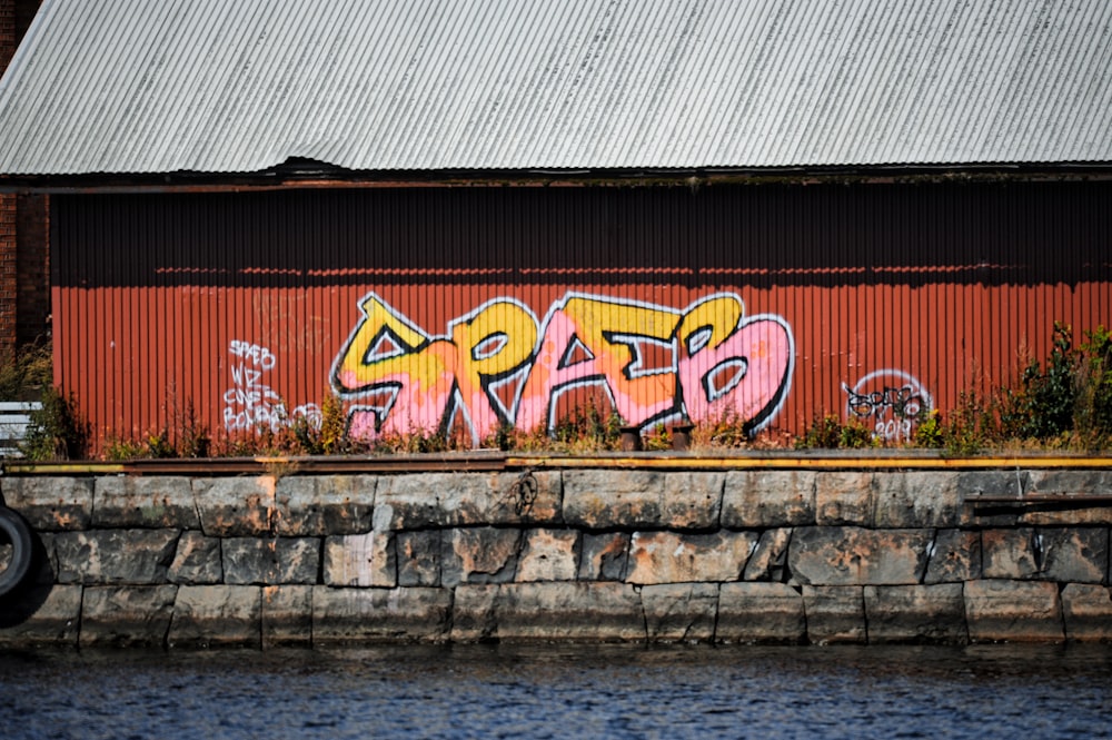 una pared de ladrillo con graffiti junto a un cuerpo de agua