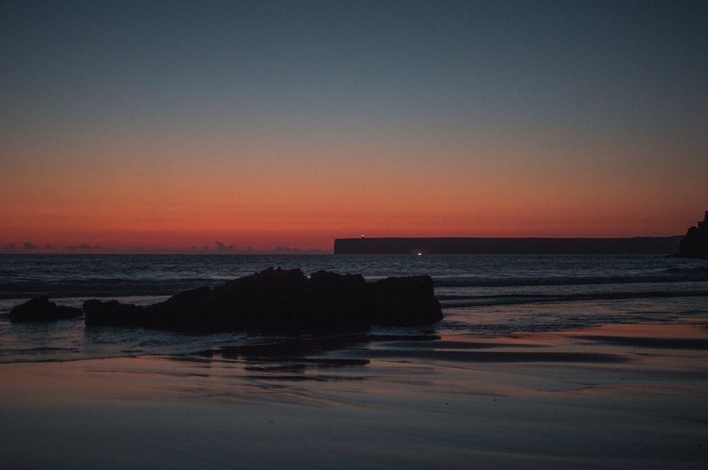 the sun is setting over the ocean with rocks in the foreground