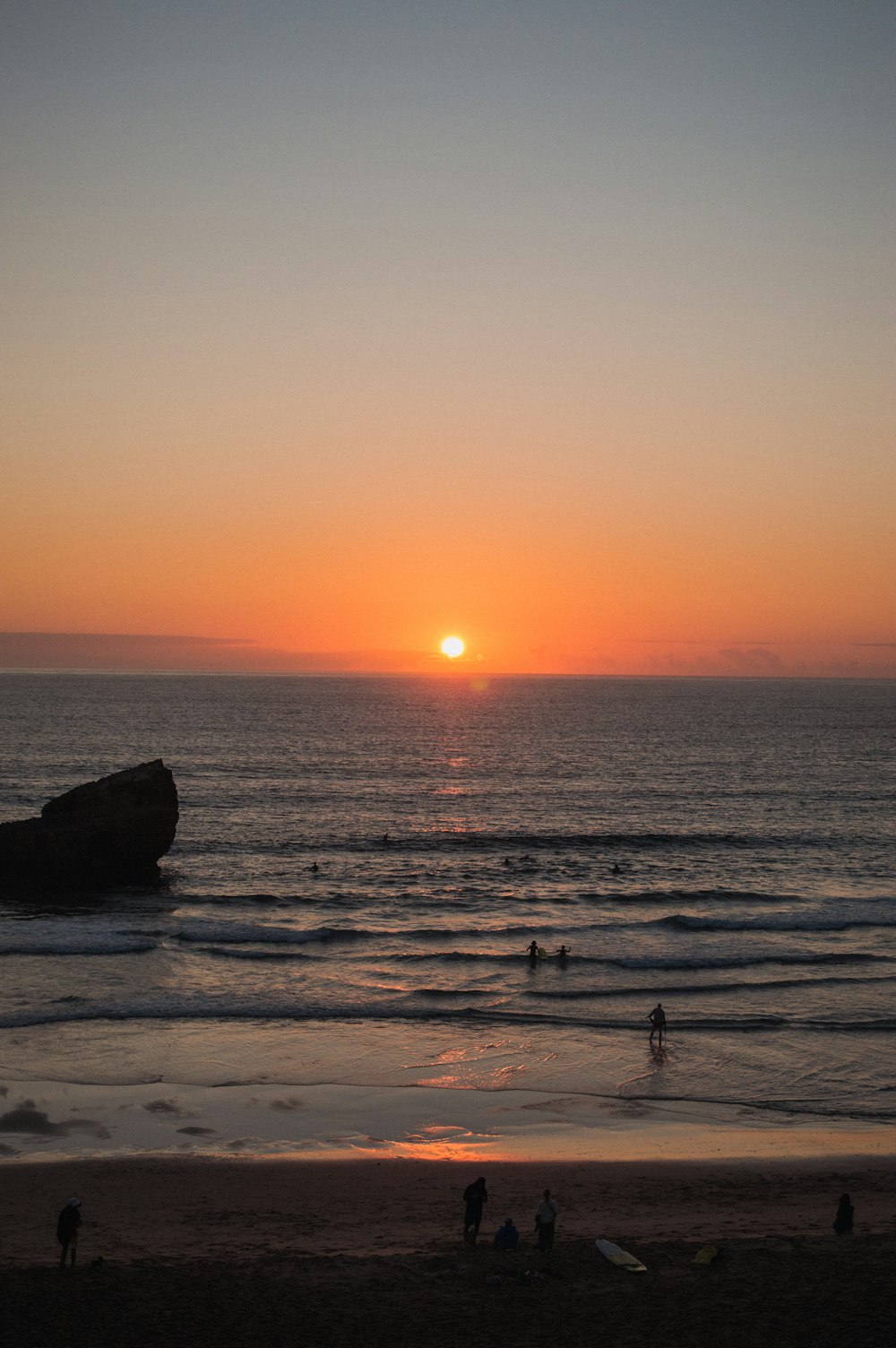 un coucher de soleil sur l’océan avec des gens sur la plage
