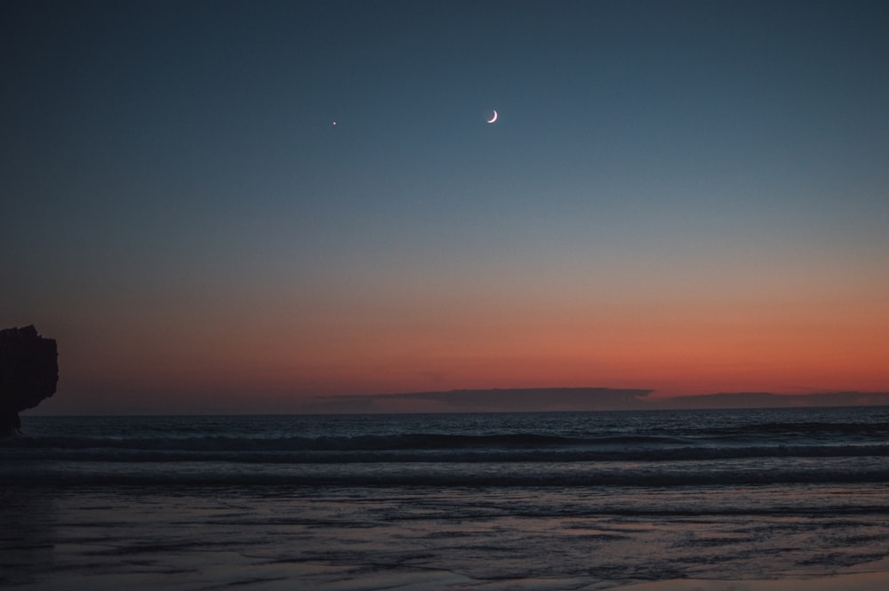 Le soleil se couche sur l’océan avec une demi-lune dans le ciel