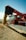 A red Massey Ferguson combine harvester unloading a large amount of grain from its chute into a growing pile in a field under a clear blue sky.