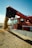 A red Massey Ferguson combine harvester unloading a large amount of grain from its chute into a growing pile in a field under a clear blue sky.