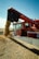 A red Massey Ferguson combine harvester unloading a large amount of grain from its chute into a growing pile in a field under a clear blue sky.