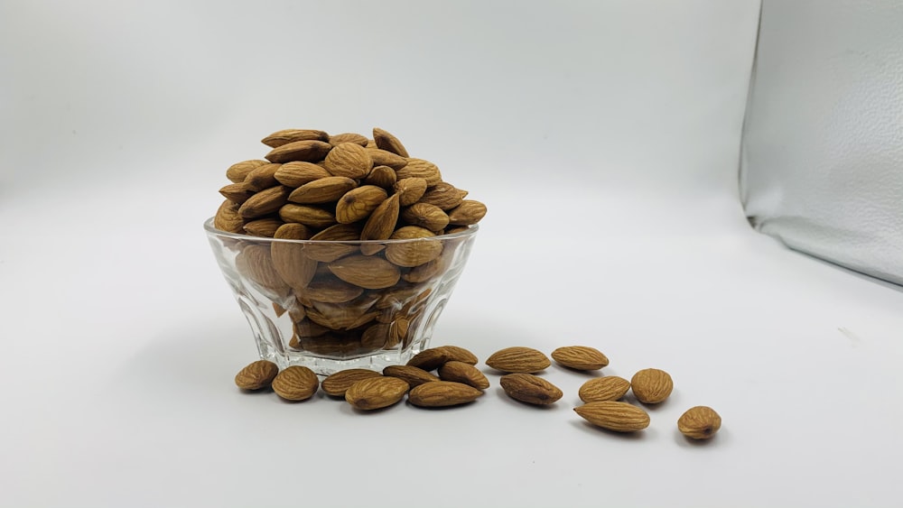 a glass bowl filled with almonds on a white surface