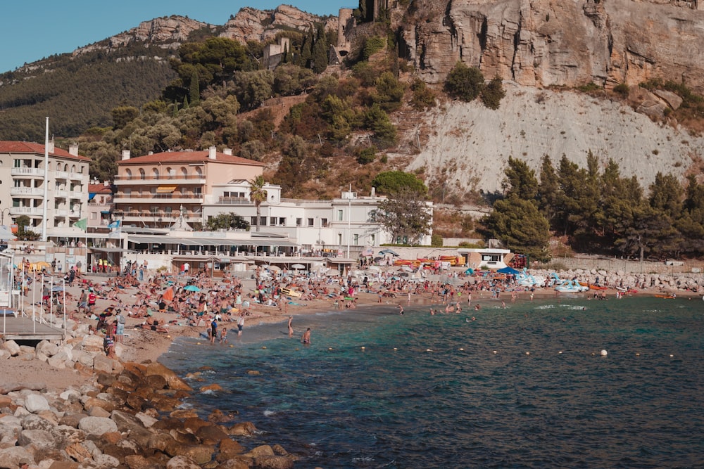 a crowded beach next to a mountain with people on it