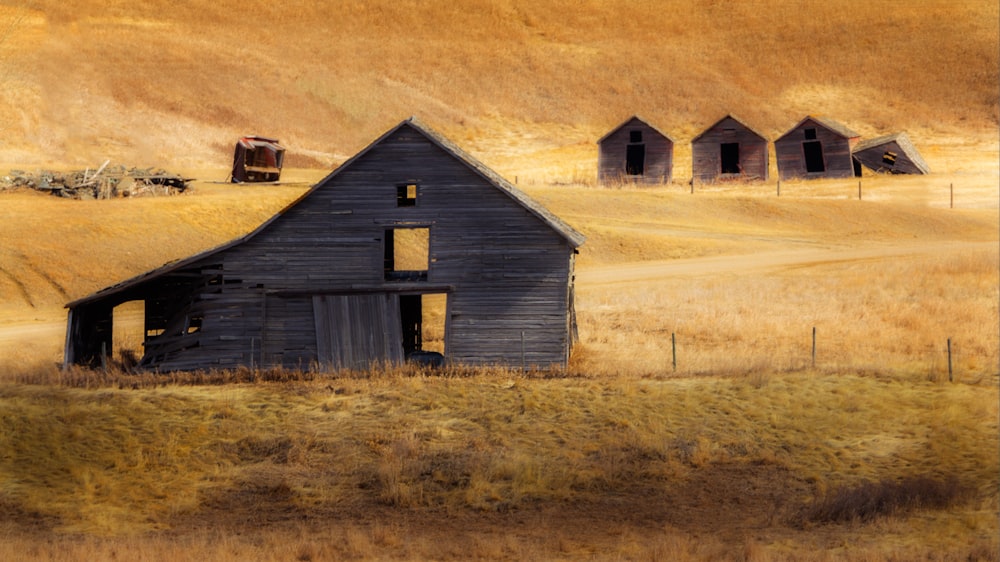 an old barn sits in a field of dry grass