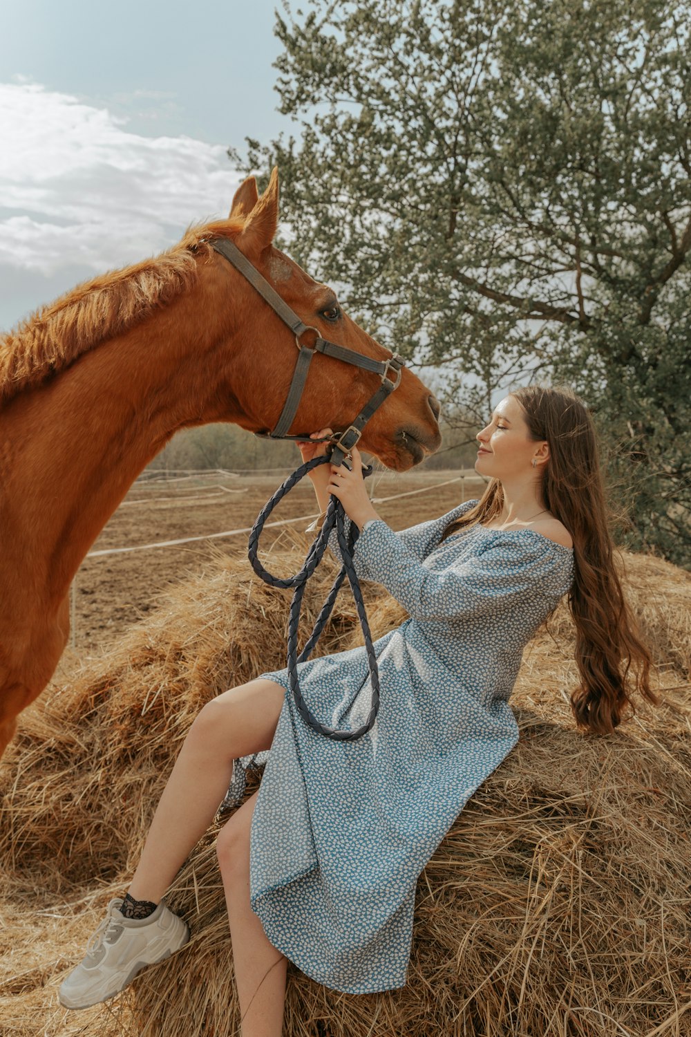 a woman sitting on a pile of hay next to a horse