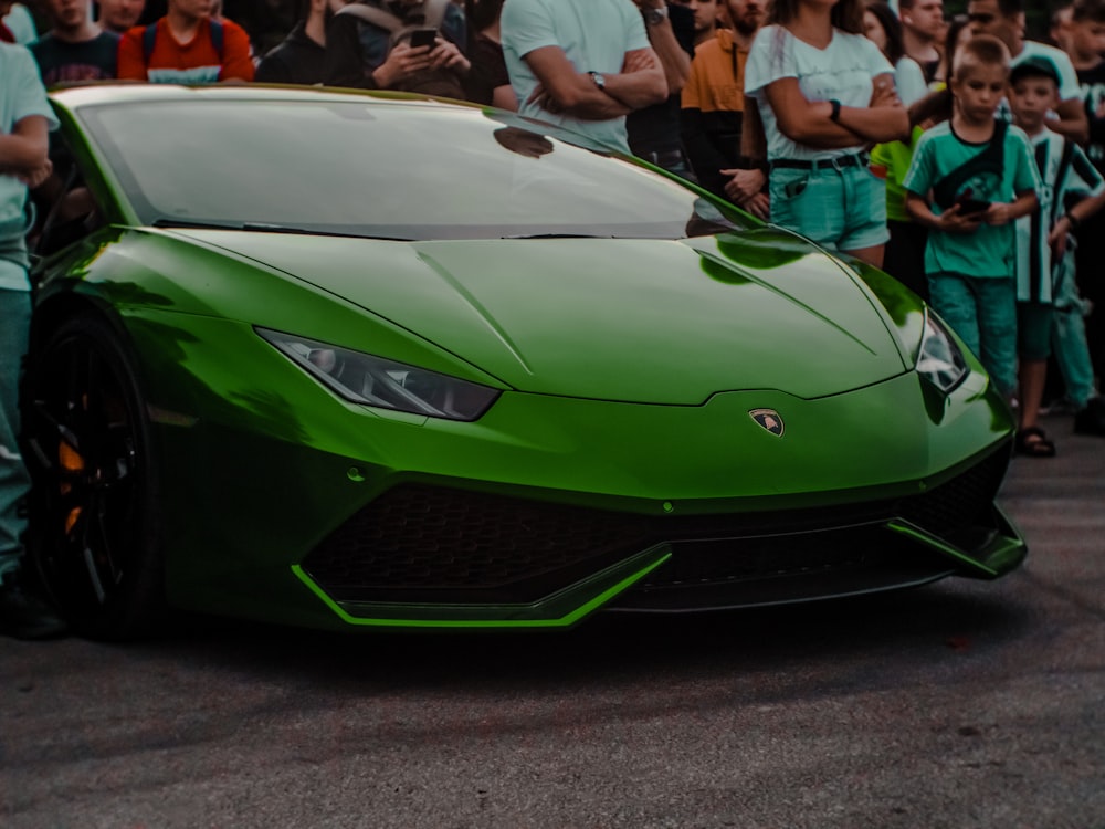 a large group of people standing around a green sports car