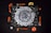 A mandala-like geometric pattern is featured on a dark background, surrounded by various orange-colored tools and objects. Items such as a stapler, tape measure, paintbrushes, a paint roller, and a small bowl complement the design. The central artwork consists of intricate white shapes arranged radially, resembling a spiral.