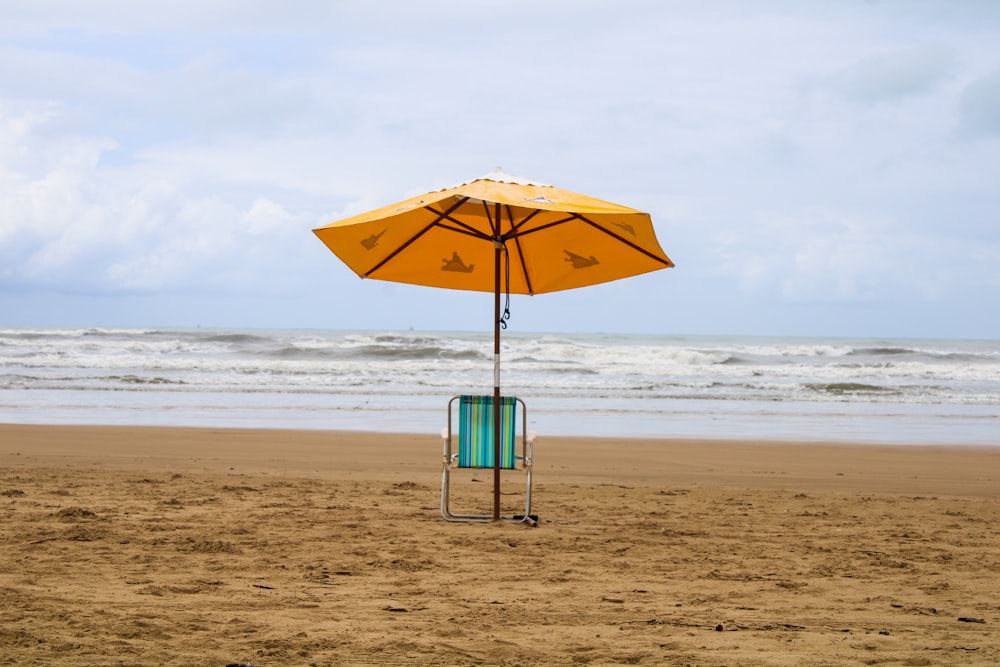 a yellow umbrella and a blue chair on a beach
