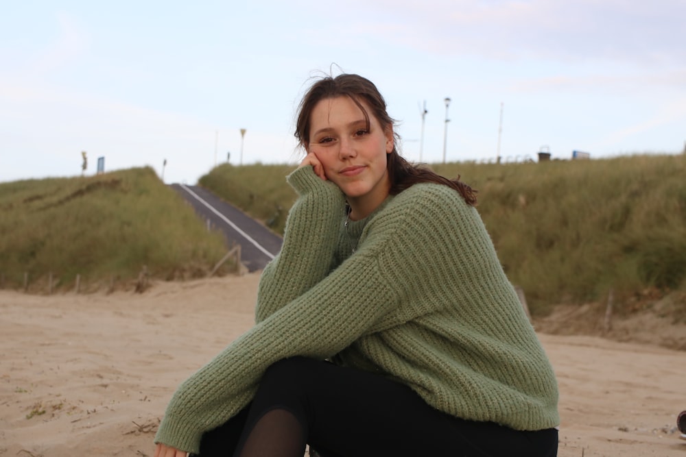 a woman in a green sweater sitting on a beach