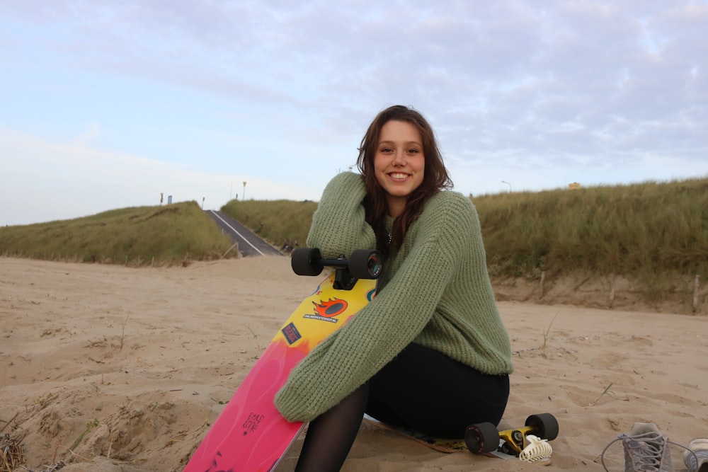 a woman kneeling on a beach holding a skateboard