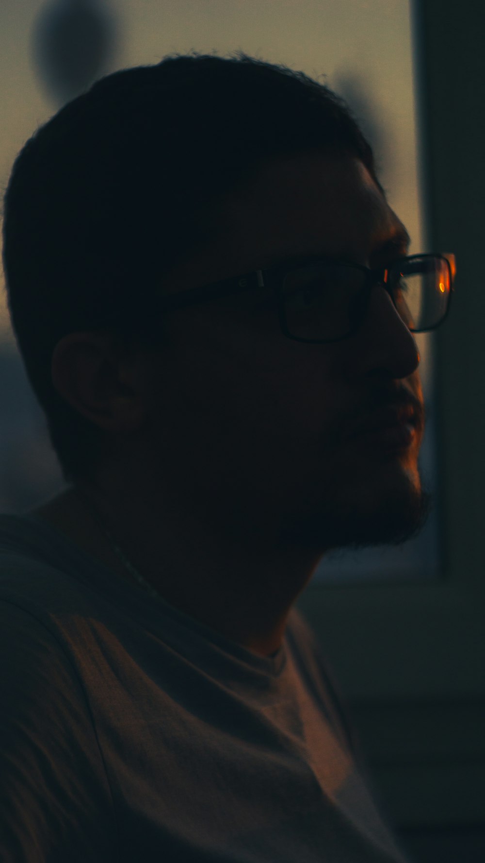 a man wearing glasses looking out a window