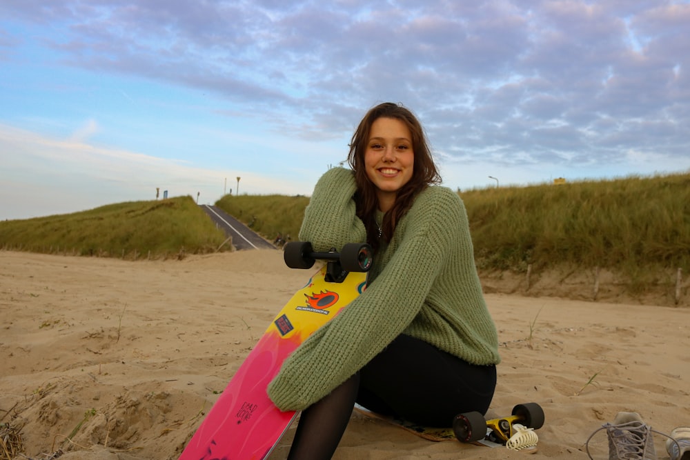 a woman sitting on a beach holding a skateboard