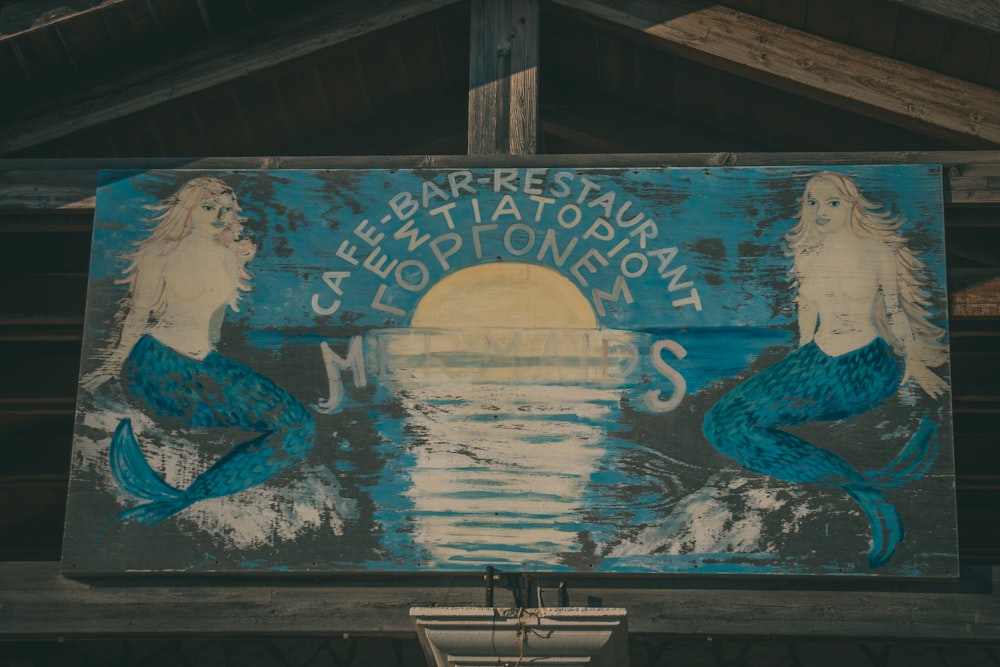 a blue sign with two mermaids painted on it
