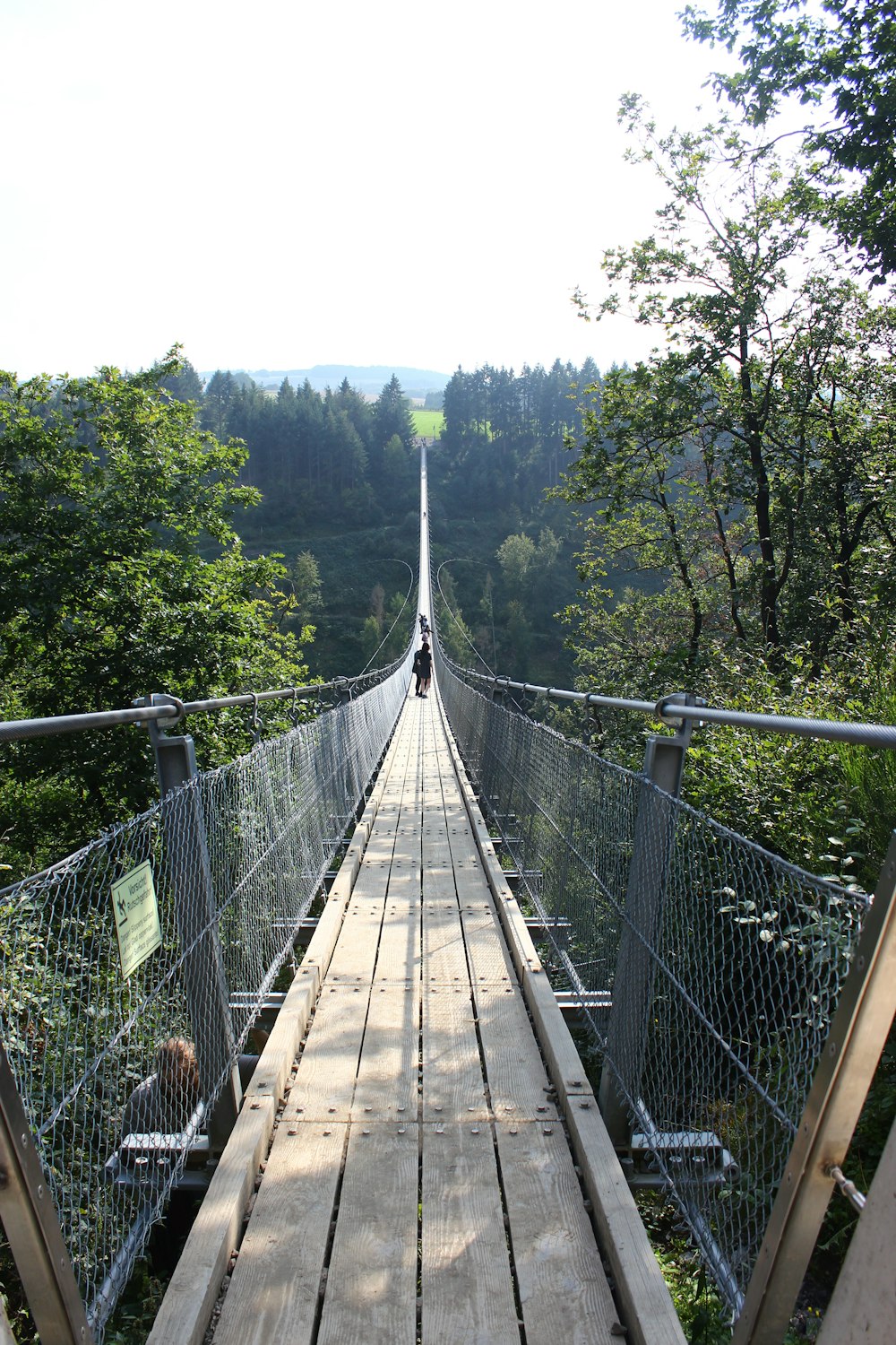 a person walking across a wooden bridge over a forest