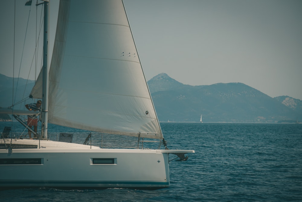 a sailboat sailing in the ocean with mountains in the background