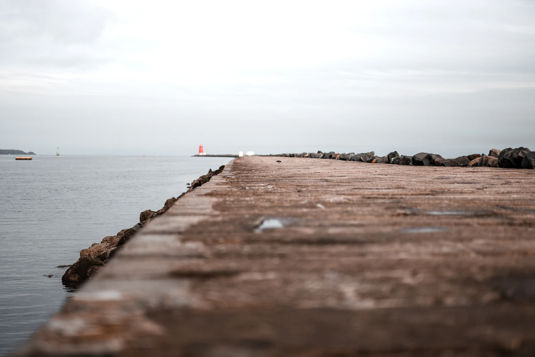 A stone harbour wall running out to a red beacon under a grey sky