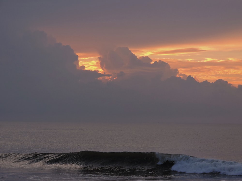 the sun is setting over the ocean with a wave coming in