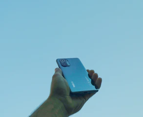 A hand holding a modern phone with a clean, minimalistic AI app screen in bright daylight.
