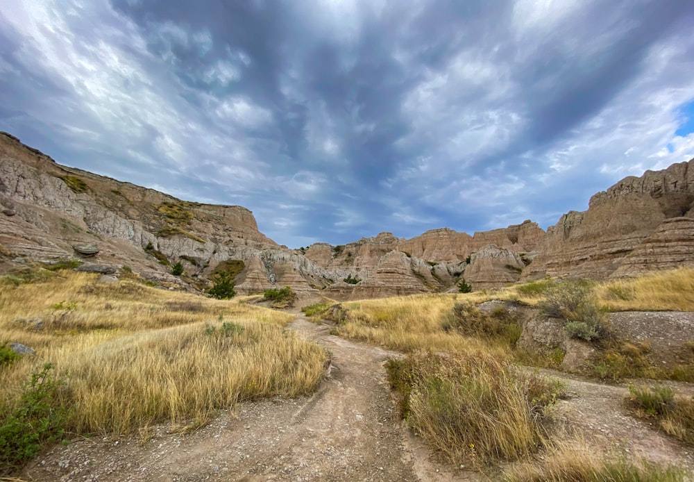 uma estrada de terra cercada por montanhas sob um céu nublado