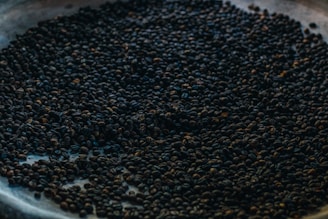 A large collection of coffee beans spread across a surface, with variations in roasting levels visible. The lighting is dim, creating a rich and earthy ambiance.