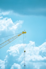 A powerful yellow crane lifting heavy steel beams at a busy construction site under a clear sky.