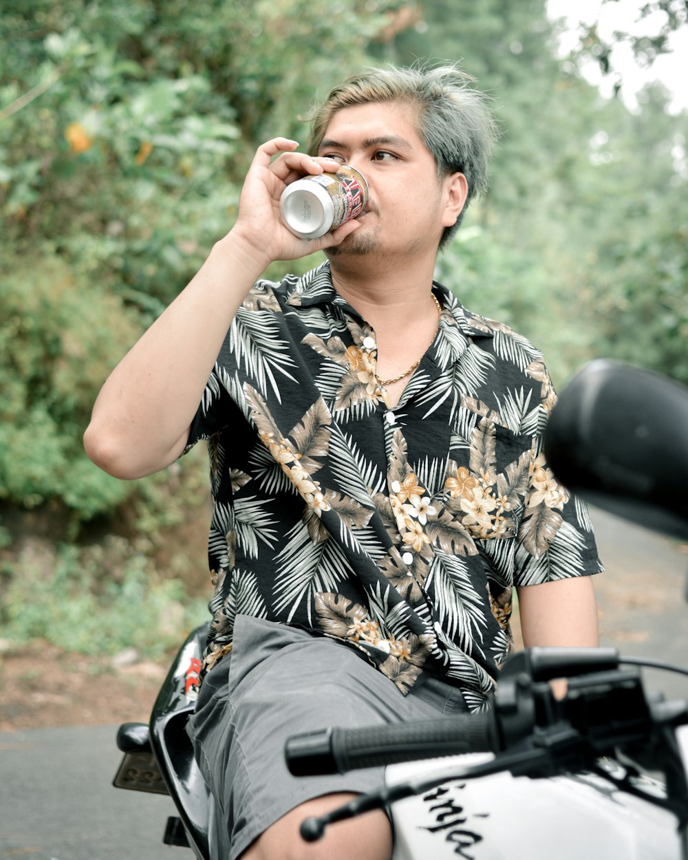a man sitting on a motorcycle drinking from a can