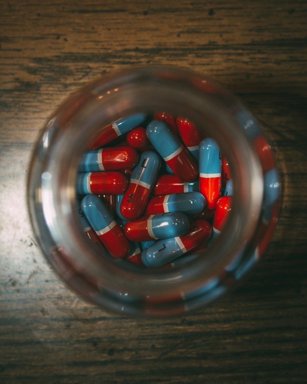 un frasco de vidrio lleno de píldoras rojas y azules
