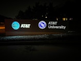 An illuminated signboard displays the AT&T logo, the wording 'AT&T University,' and an emblem with the text 'AT&T University Established 2009.' The sign is positioned outside against a background of trees, and the setting appears to be at night.