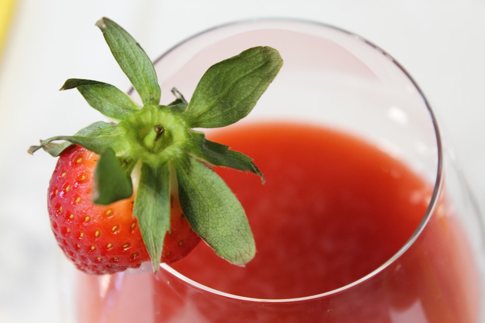 a close up of a glass of juice with a strawberry on the rim