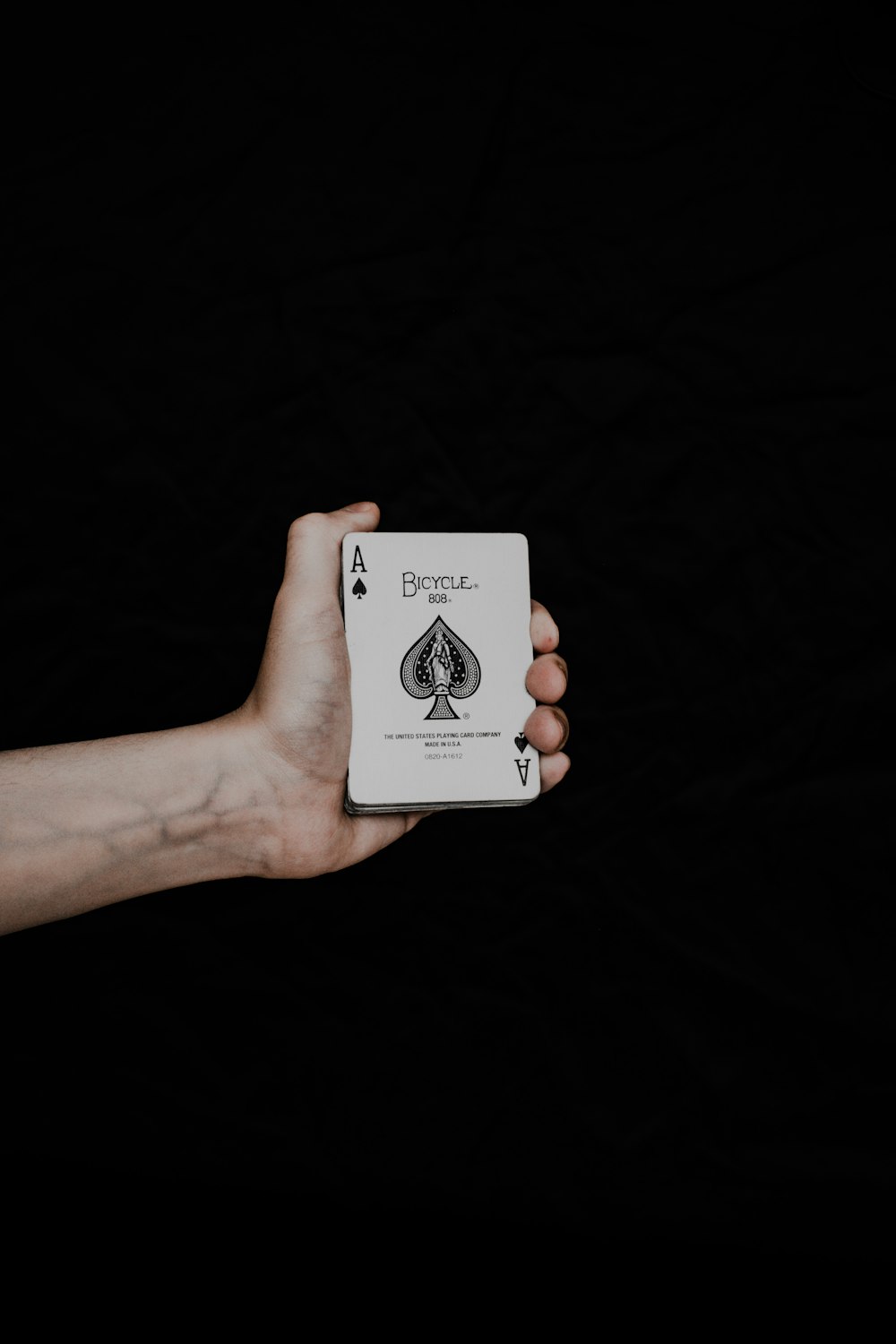 a hand holding a playing card in front of a black background