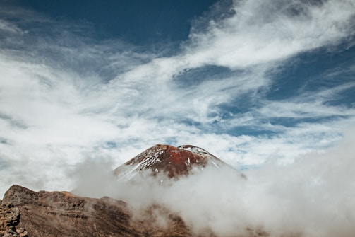 Close-up of a snow-capped mountain peak with wisps of clouds swirling around it.