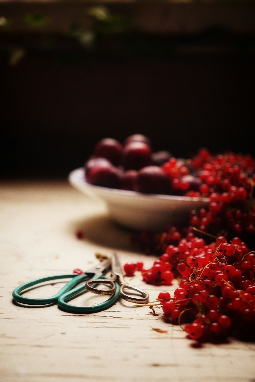 a bowl of cherries and a pair of scissors on a table